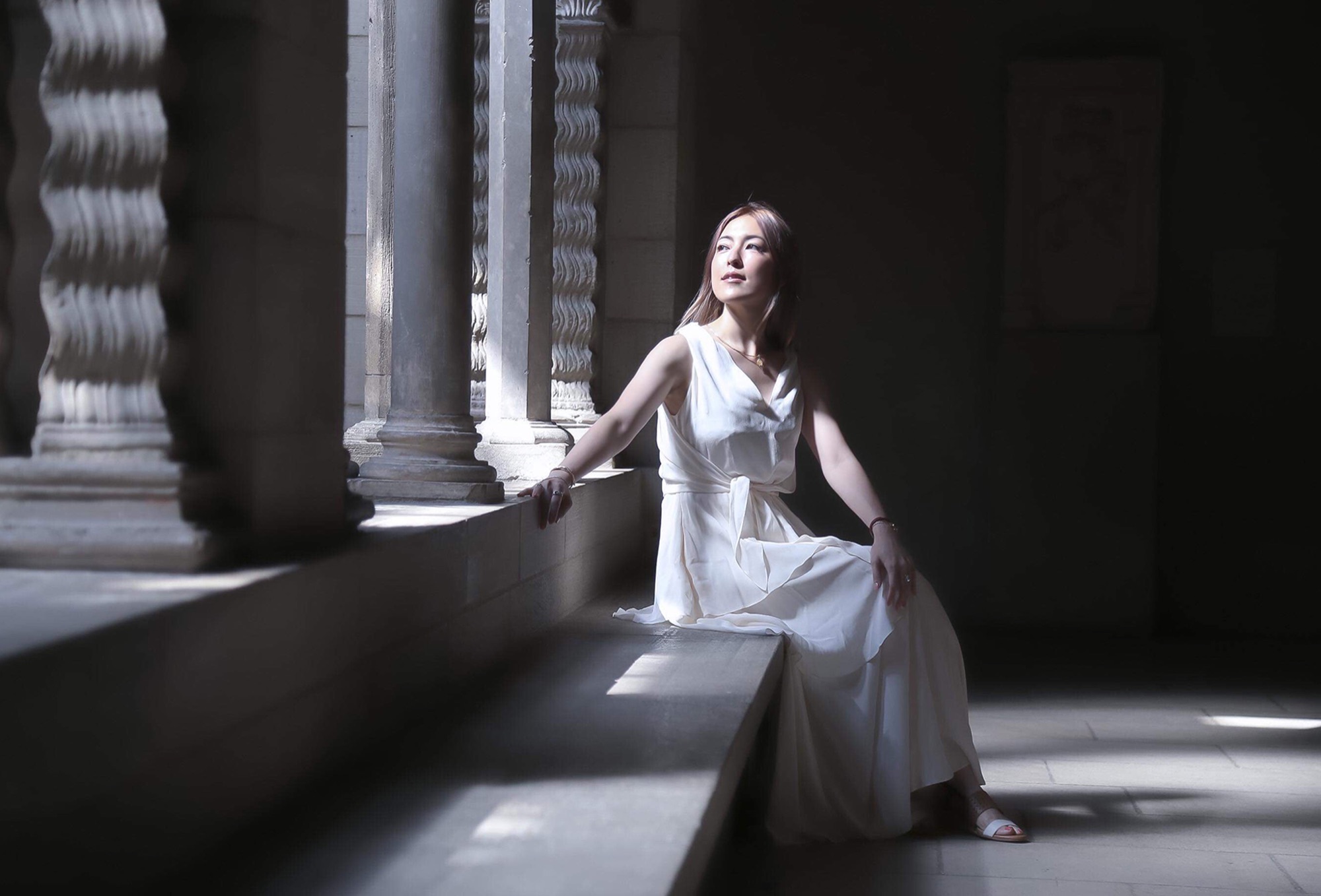 mogmin. seated in light falling across a stone cloister