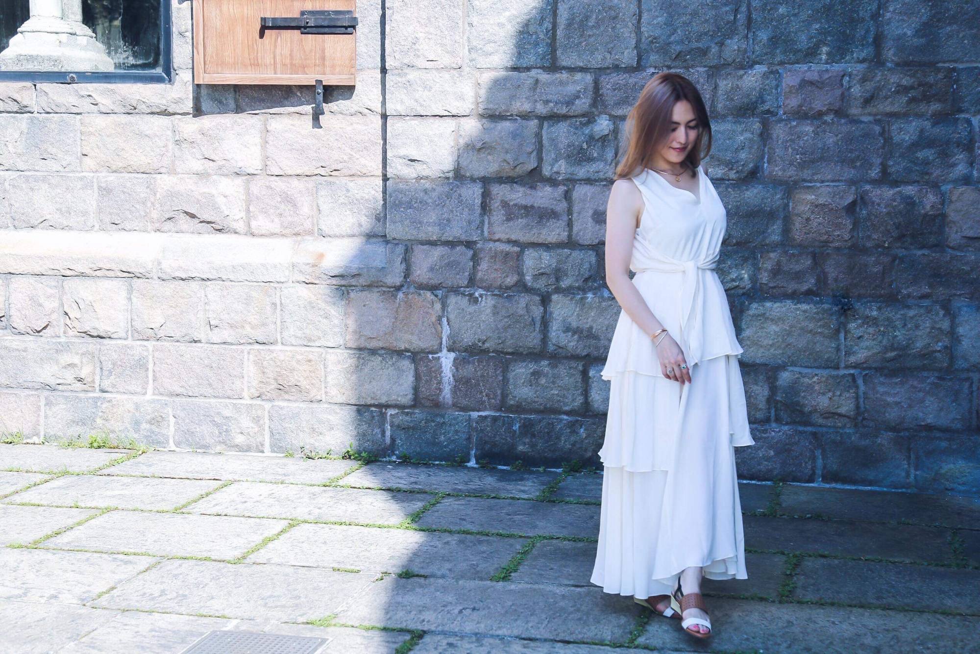 mogmin. walking past a stone wall in a white dress